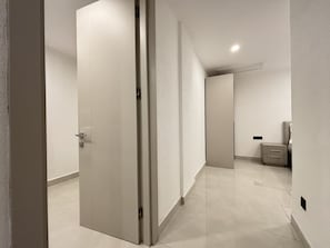 A hallway with a closed door, a small cabinet, and a bed in the distance.