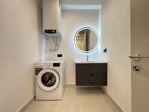 A compact bathroom with a washing machine, a sink, and a mirror. - Private Pool Villa for Groups | Türkbükü (Bodrum)