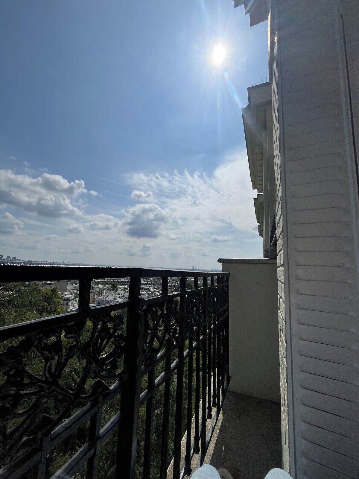 Un balcon avec vue sur le paysage urbain, un ciel dégagé et un soleil éclatant.