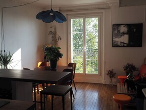 Ein Essbereich mit Tisch und Stühlen, einer Zimmerpflanze und einem großen Fenster mit Blick auf Bäume.