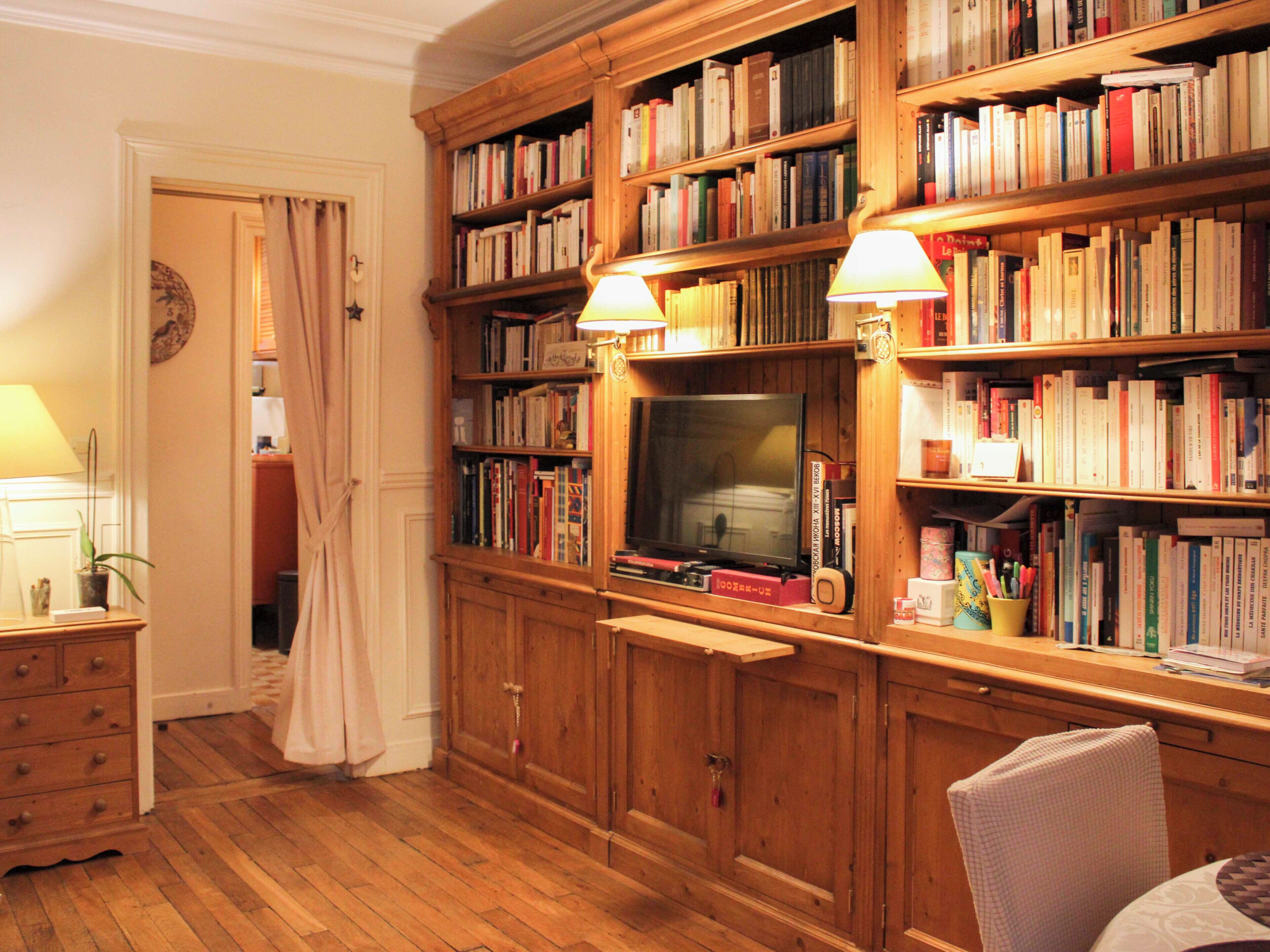 A room with wooden bookshelves filled with books, a television, and a desk with a lamp.