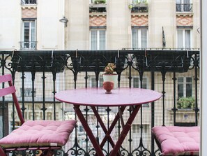 Ein Balkon mit rundem Tisch, zwei gepolsterten Stühlen und einem Blumentopf.