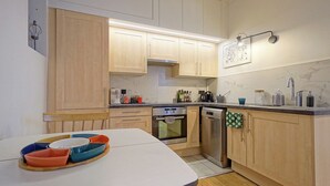 A compact kitchen with wooden cabinets, a built-in oven, a dishwasher, and a countertop with various kitchen items. - Charming Well Purified Studio Near Sacre Coeur (Paris)