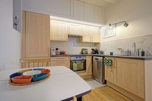 A compact kitchen with wooden cabinets, a built-in oven, a dishwasher, and a countertop with various kitchen items. - Charming Well Purified Studio Near Sacre Coeur (Paris)