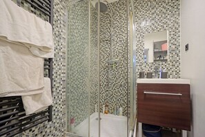 A bathroom with a glass-enclosed shower, a white sink, and a mirror above the sink. - Charming Well Purified Studio Near Sacre Coeur (Paris)