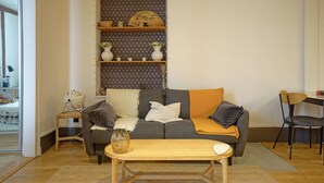A living room with a sofa, a coffee table, a bookshelf, and a chair. - Charming Well Purified Studio Near Sacre Coeur (Paris)