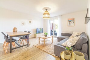 Een moderne woonkamer met een eethoek, een zithoek, een televisie en een poster aan de muur.