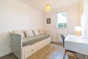 Een kamer met een bed, een bureau, een stoel, een raam en een hanglamp.