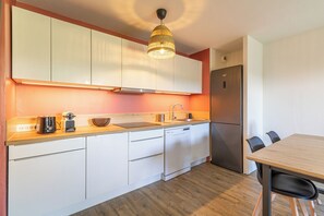 A compact kitchen with white cabinets, a built-in dishwasher, a stainless steel refrigerator, and a wooden dining table with chairs. - Le Diamant - Bright apartment with pool (Toulouse)
