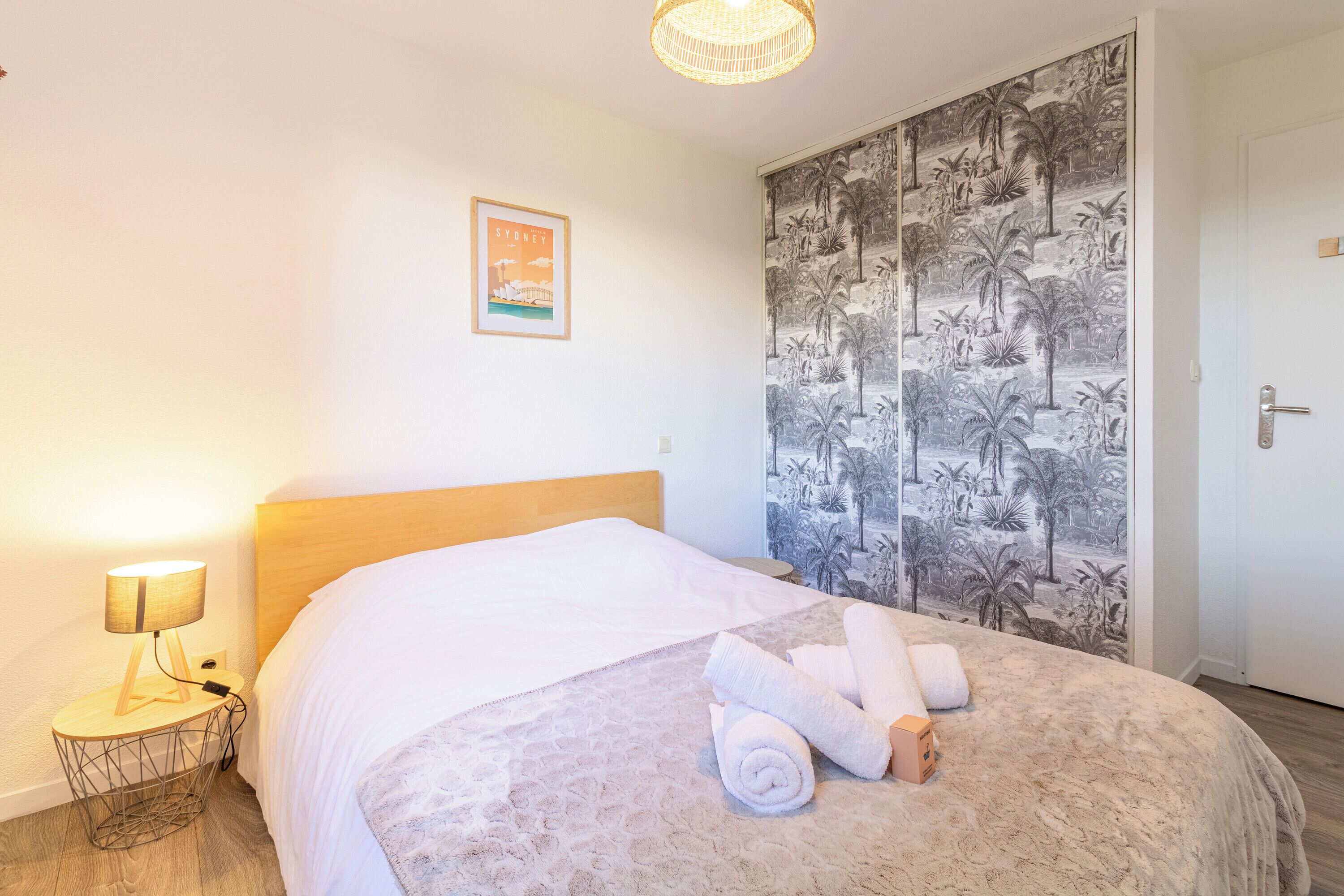 Une chambre d’hôtel avec un lit, une table de chevet, une lampe, un tableau encadré et une porte.