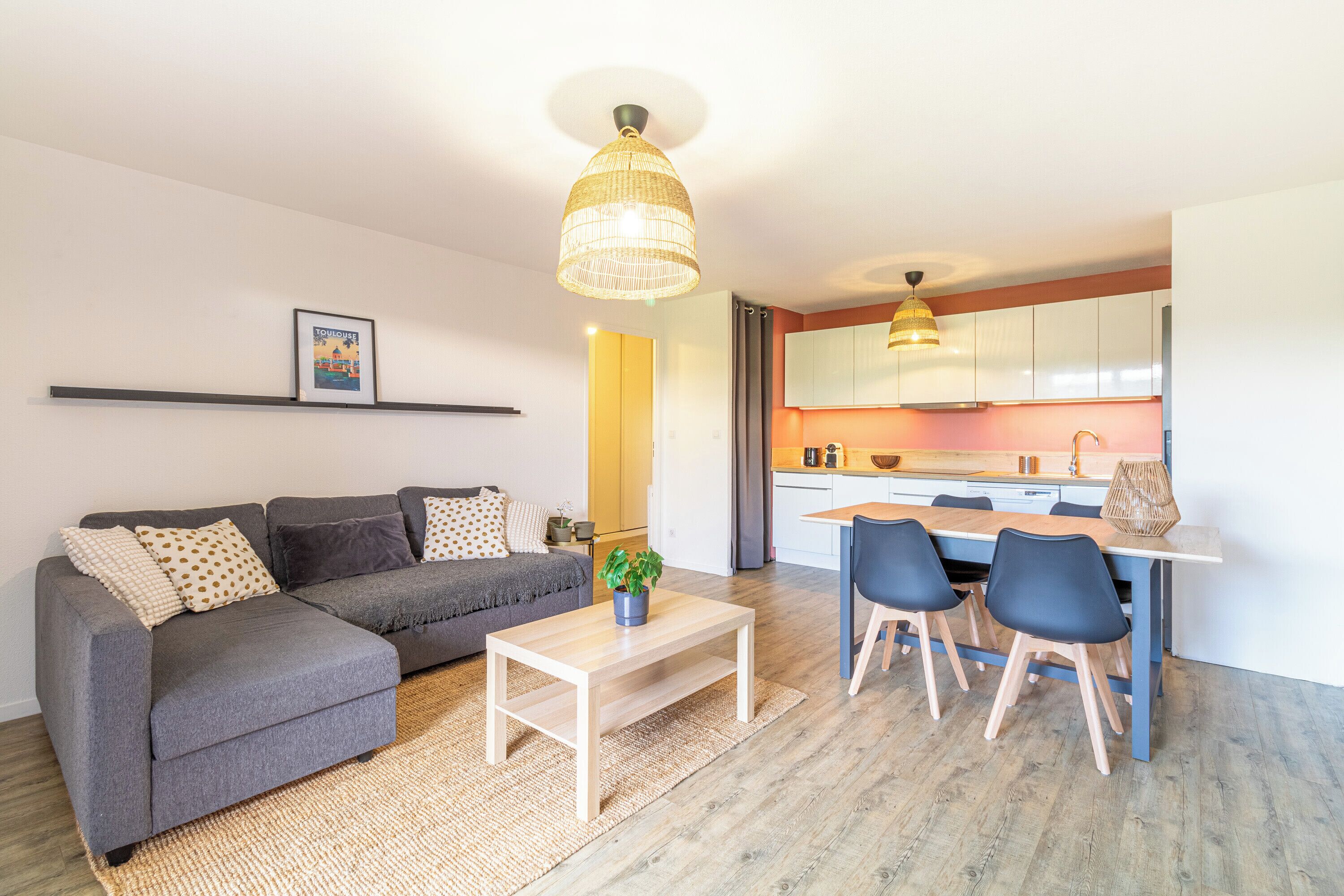 A modern living room with a grey sofa, a wooden coffee table, and a dining area with a table and chairs.