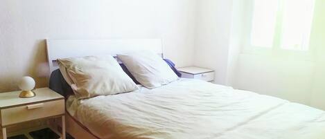 Una cama individual con ropa blanca, una mesita de noche con una lámpara y un atril con un teléfono.