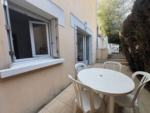 Eine Terrasse mit einem runden Tisch und Stühlen, eine Schiebetür aus Glas und ein weißer Zaun im Hintergrund.
