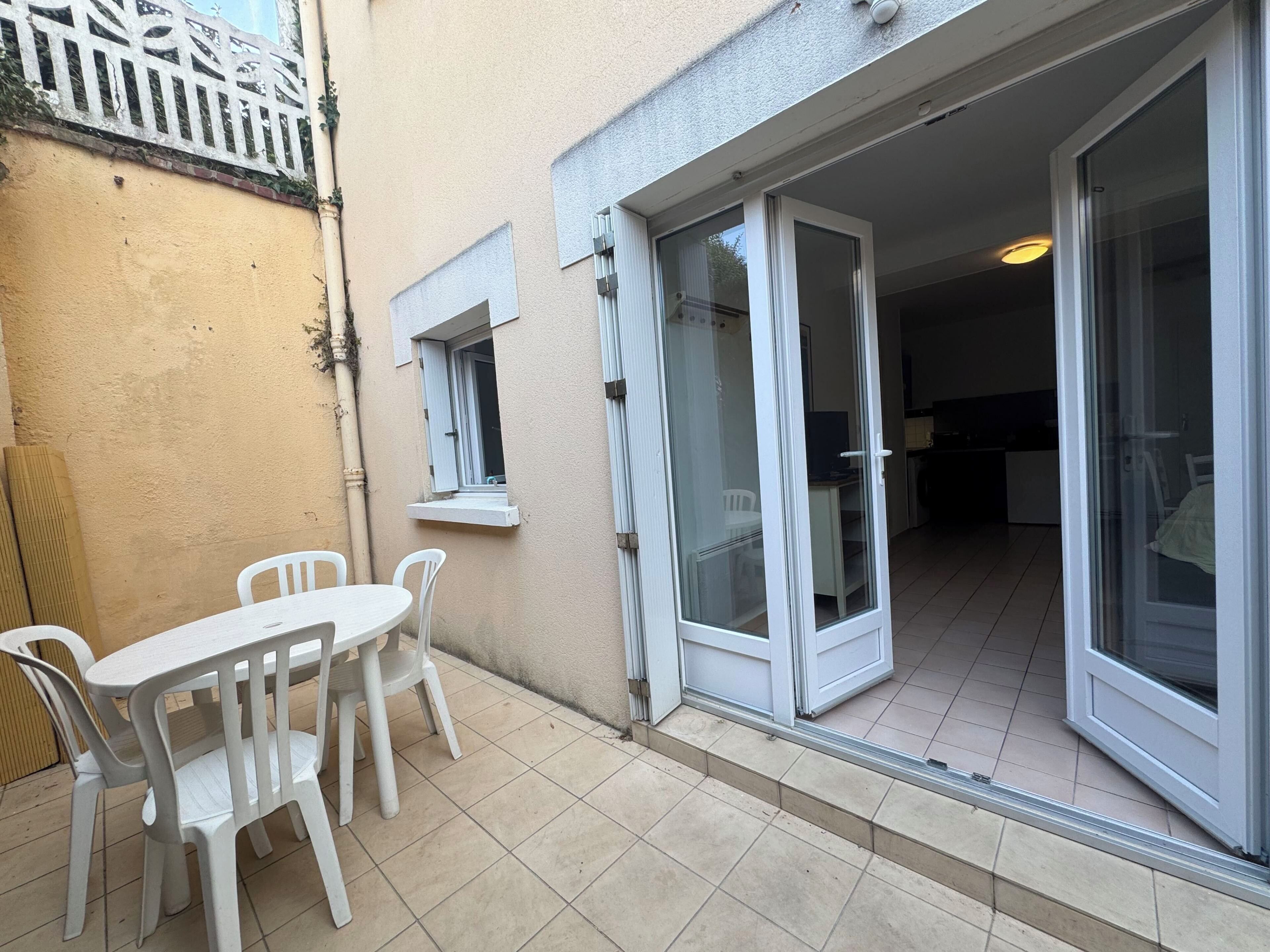 A small patio with a table and chairs, a sliding glass door leading to an interior space, and a small window.