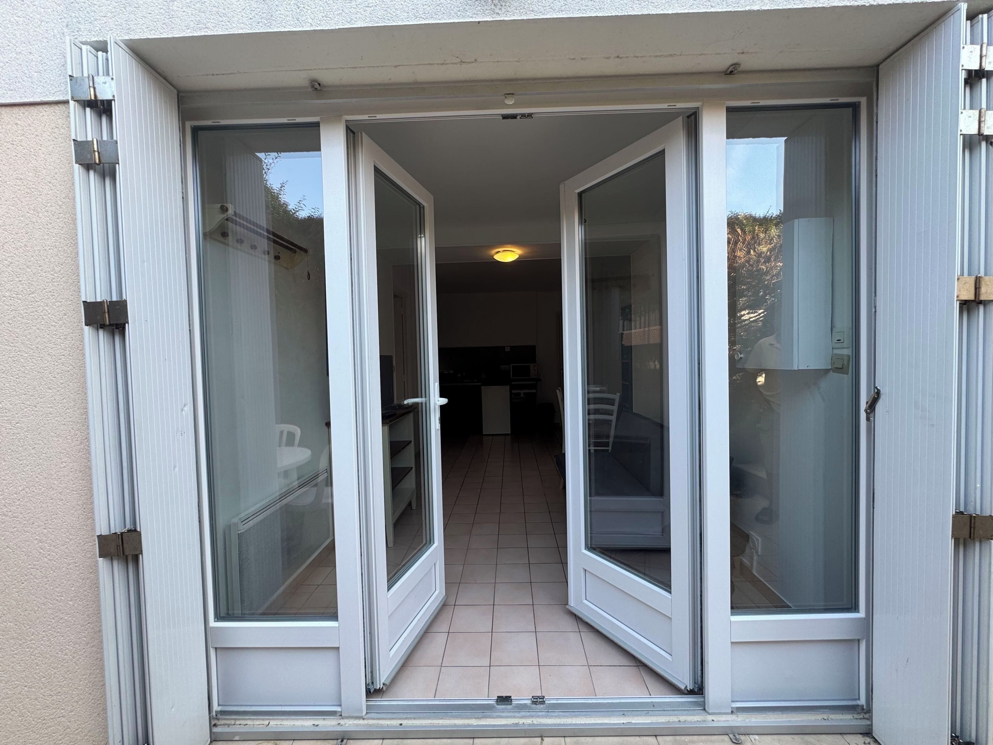 Une porte-fenêtre coulissante donne accès à un balcon doté d’un sol carrelé et offrant une vue sur un espace intérieur comprenant une cuisine et un coin repas.