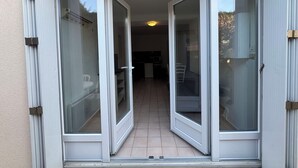 A sliding glass door leading to a balcony with a tiled floor and a view of an interior space with a kitchen and dining area. - Ground floor apart, walking distance to the beach (Cabourg)