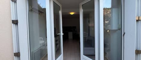 Een schuifdeur leidt naar een balkon met een betegelde vloer en uitzicht op een binnenruimte met een keuken en een eetgedeelte.