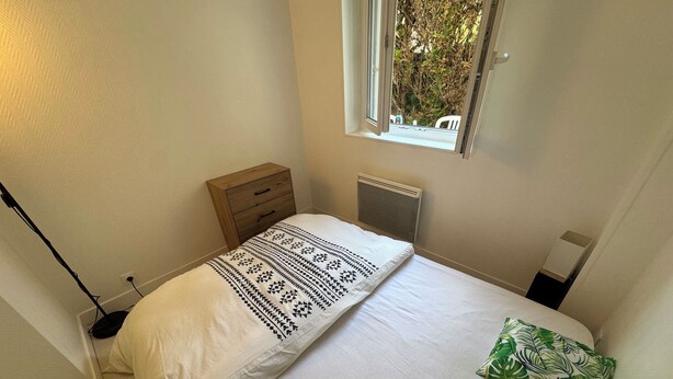 A bedroom with a bed, a nightstand, a window, and a radiator. - Ground floor apart, walking distance to the beach (Cabourg)