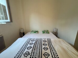 Ein Bett mit einem gemusterten Überwurf, zwei Kissen, Nachttischlampen und ein Fenster.