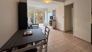 A dining area with a table and chairs, a television, and a view through a glass door to an outdoor area. - Ground floor apart, walking distance to the beach (Cabourg)