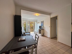 A dining area with a table and chairs, a television, and a view through a glass door to an outdoor area. - Ground floor apart, walking distance to the beach (Cabourg)