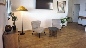 A modern living room with two patterned armchairs, a small round table, a floor lamp, and a flat-screen TV mounted on the wall. - Sea view apartment, Sanguinaires Islands terraces (Ajaccio)