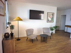 Ein modernes Wohnzimmer mit zwei gemusterten Sesseln, einem kleinen runden Tisch, einer Stehlampe und einem flachbildfernseher an der Wand.
