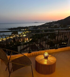 Ein Balkon mit Blick auf das Meer und die Stadtlandschaft im Abendlicht.