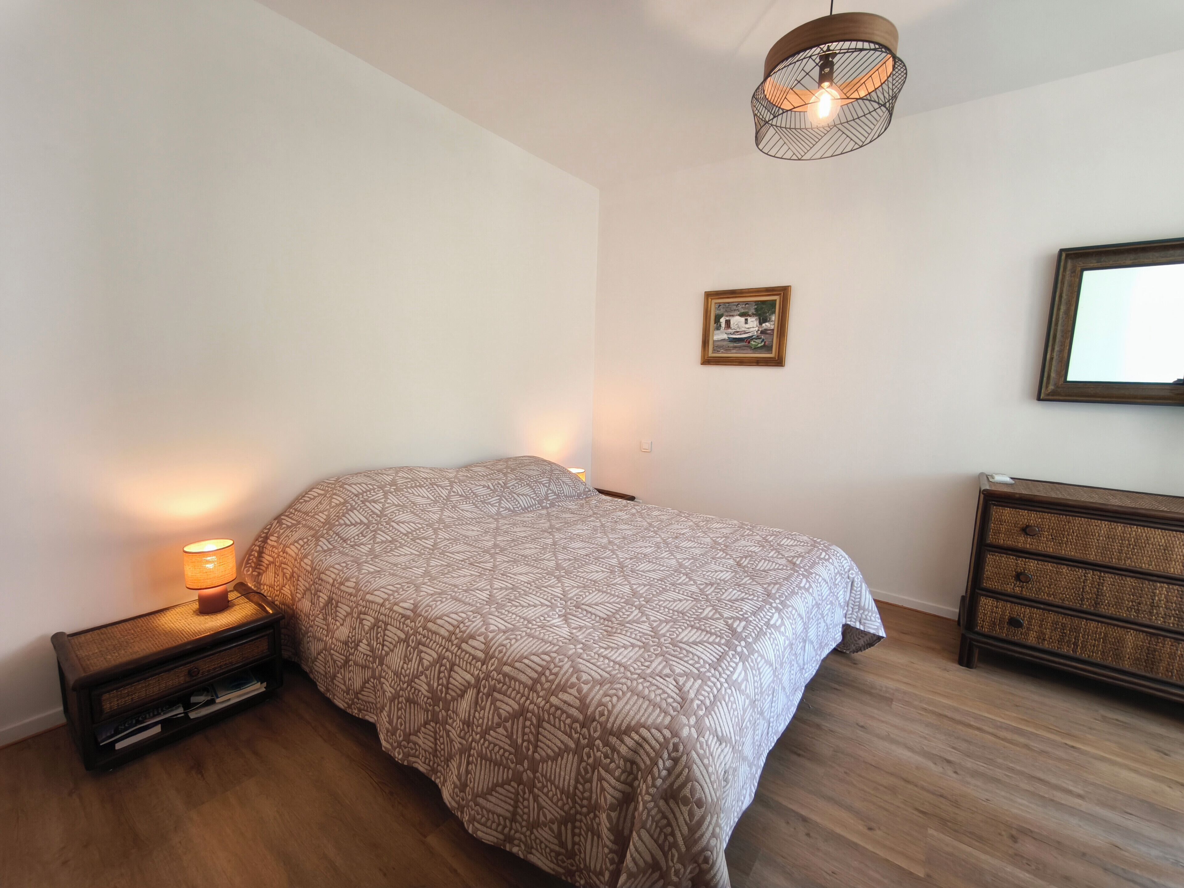 A bedroom with a bed, bedside lamp, dresser, and a hanging light fixture.
