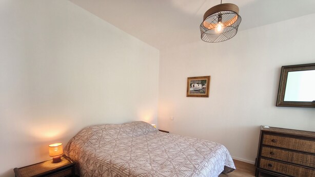 A bedroom with a bed, bedside lamp, dresser, and a hanging light fixture. - Sea view apartment, Sanguinaires Islands terraces (Ajaccio)