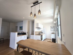 Eine moderne Küche mit Esstisch aus Holz, weißen Schränken und Pendelleuchten.