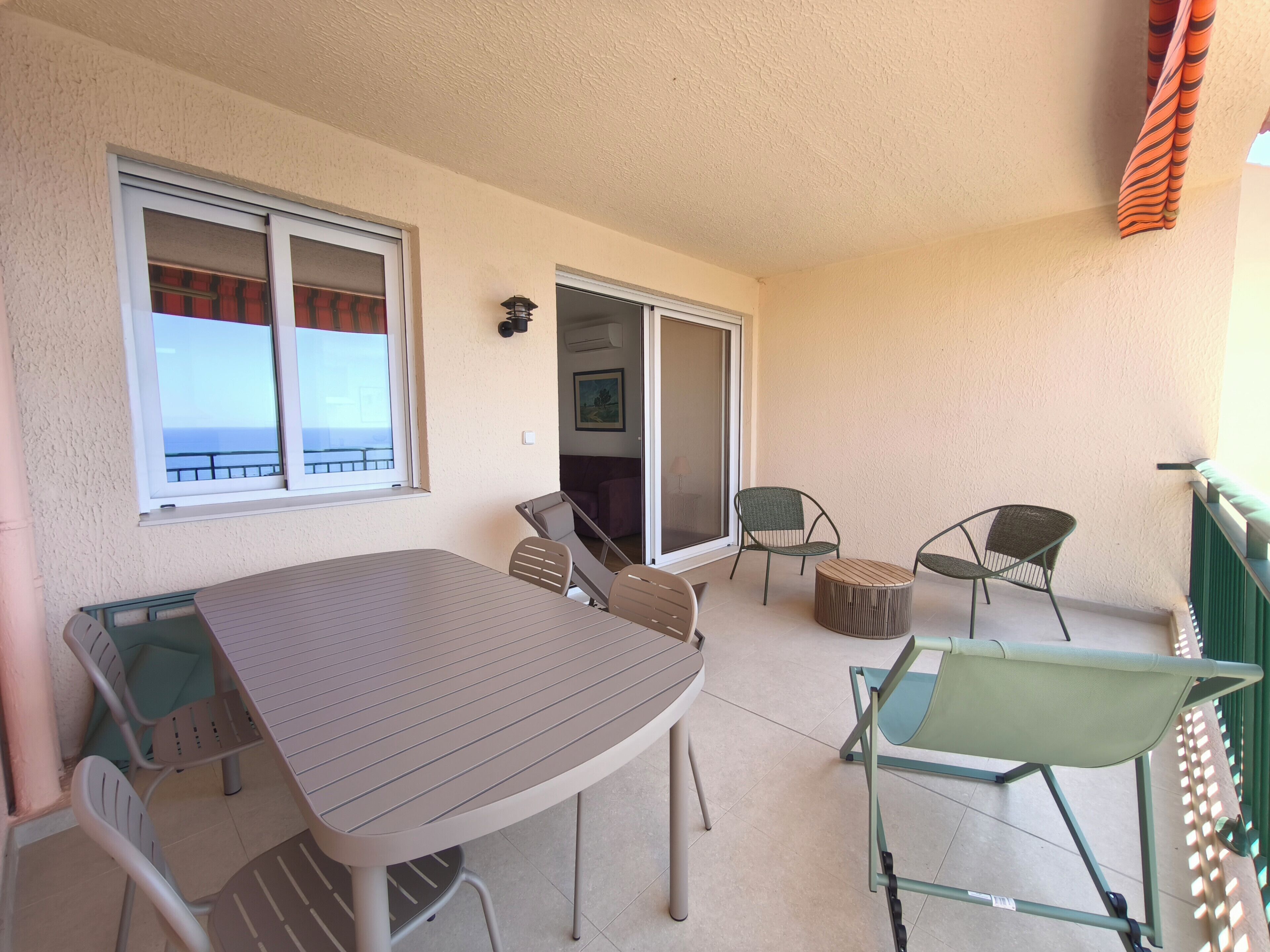 Un balcon avec une table et des chaises, une porte coulissante et une vue sur la mer.