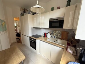 A compact kitchen with white cabinets, a black oven, a stainless steel microwave, and a wooden countertop. - Large, quiet apartment with balcony in Paris 12 (Paris)