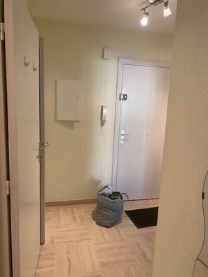 A hallway with a white door, a small trash bin, and a light switch on the wall. - Apartment with shared pool and terrace (Mandelieu-la-Napoule)