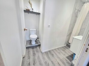 Ein Badezimmer mit Toilette, Dusche und Ablagefläche mit Vase und Tassen.