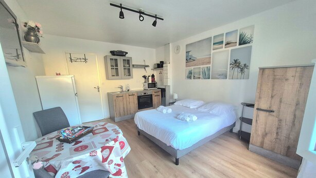 Een kleine kamer met een bed, een eettafel, een kitchenette en een kledingkast.