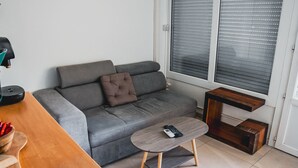 En moderne stue med en grå sofa, et lille træbord og et vindue med persienner.