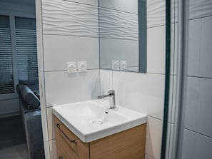 Ein Badezimmer mit weißem Waschbecken, Holzschrank und Spiegel mit wellenförmigem Fliesendekor.