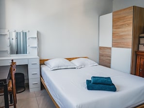 Ein Schlafzimmer mit einem Bett, einem Holzkopfende, einem Schreibtisch mit Spiegel und einem Kleiderschrank.