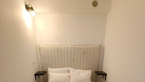 Una cama individual con cabecera, dos mesitas de noche y una lámpara fijada en la pared.