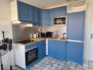 A compact kitchen with blue cabinets, a microwave, a stove, and a sink. - Apartment with sea view, terrace and swimming pool (Antibes)
