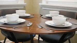 Une table de salle à manger ronde, avec quatre bols et assiettes blancs, des couverts en argent et des chaises noires.