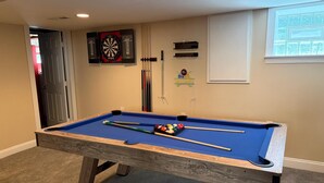 Une table de billard avec des billes et des queues de billard, un jeu de fléchettes et un porte-billes adossé à un mur.