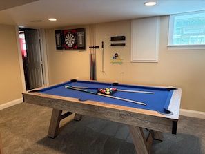 Ein Billardtisch mit Billardkugeln und Spielstöcken, eine Dartscheibe und ein Billardständer an einer Wand.