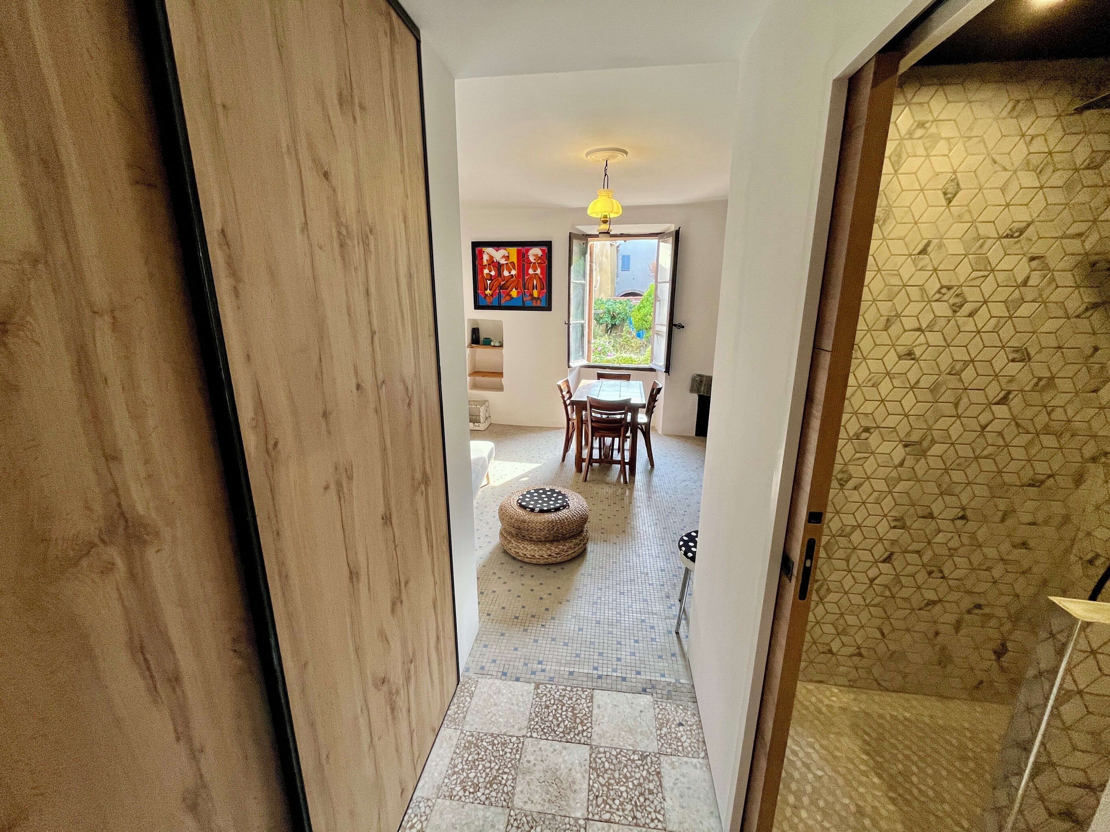 A hallway leading to a dining area with a table and chairs, a patterned floor, and a wall with a geometric design.
