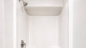 Une douche à l’italienne blanche et vide, équipée d’un pommeau de douche et d’un drain.