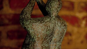 Une sculpture en bronze représentant une figure humaine les bras tendus, suspendue devant un mur en briques.