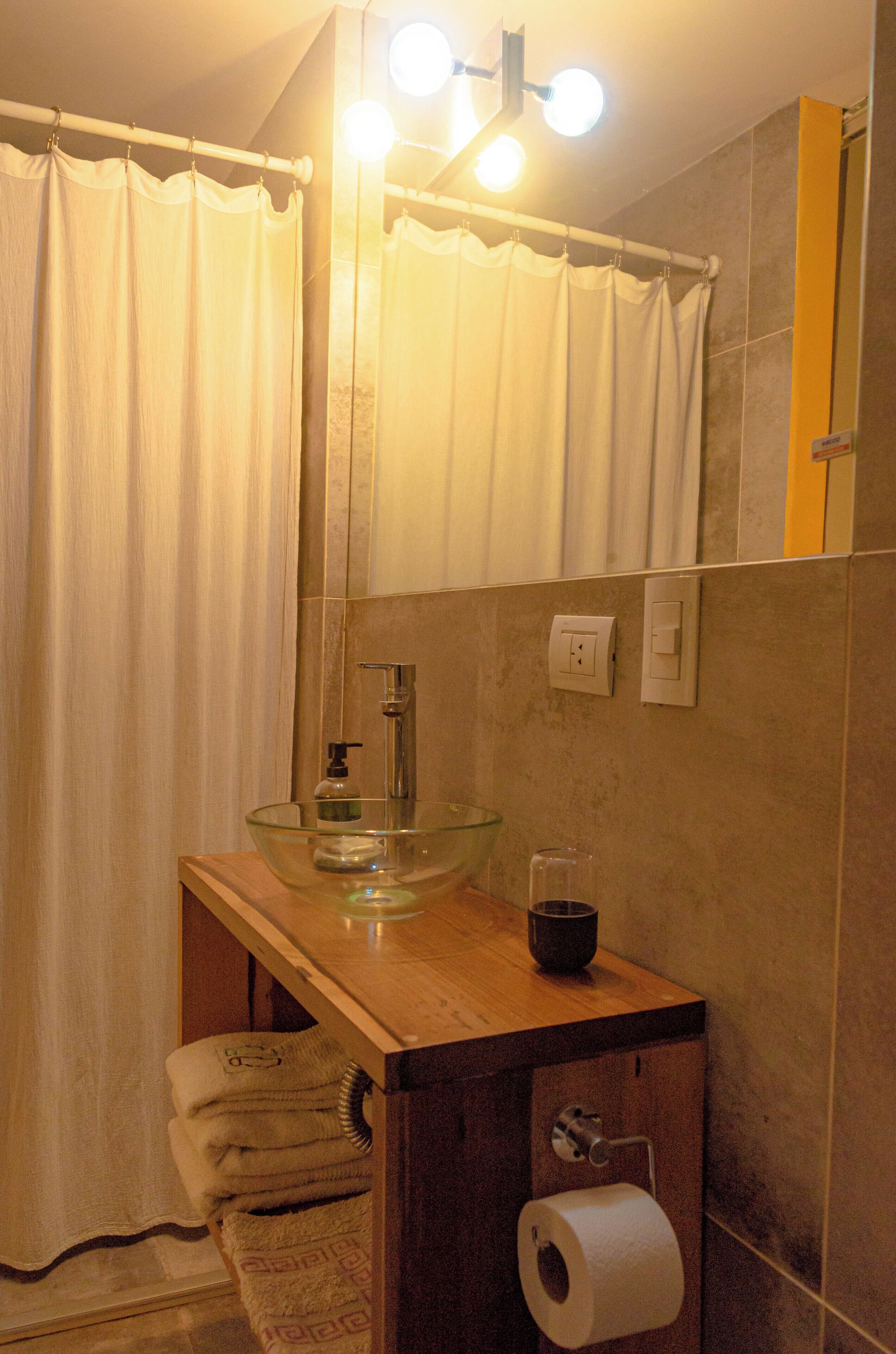 A bathroom with a glass sink, a towel rack, a mirror, and a toilet paper holder.
