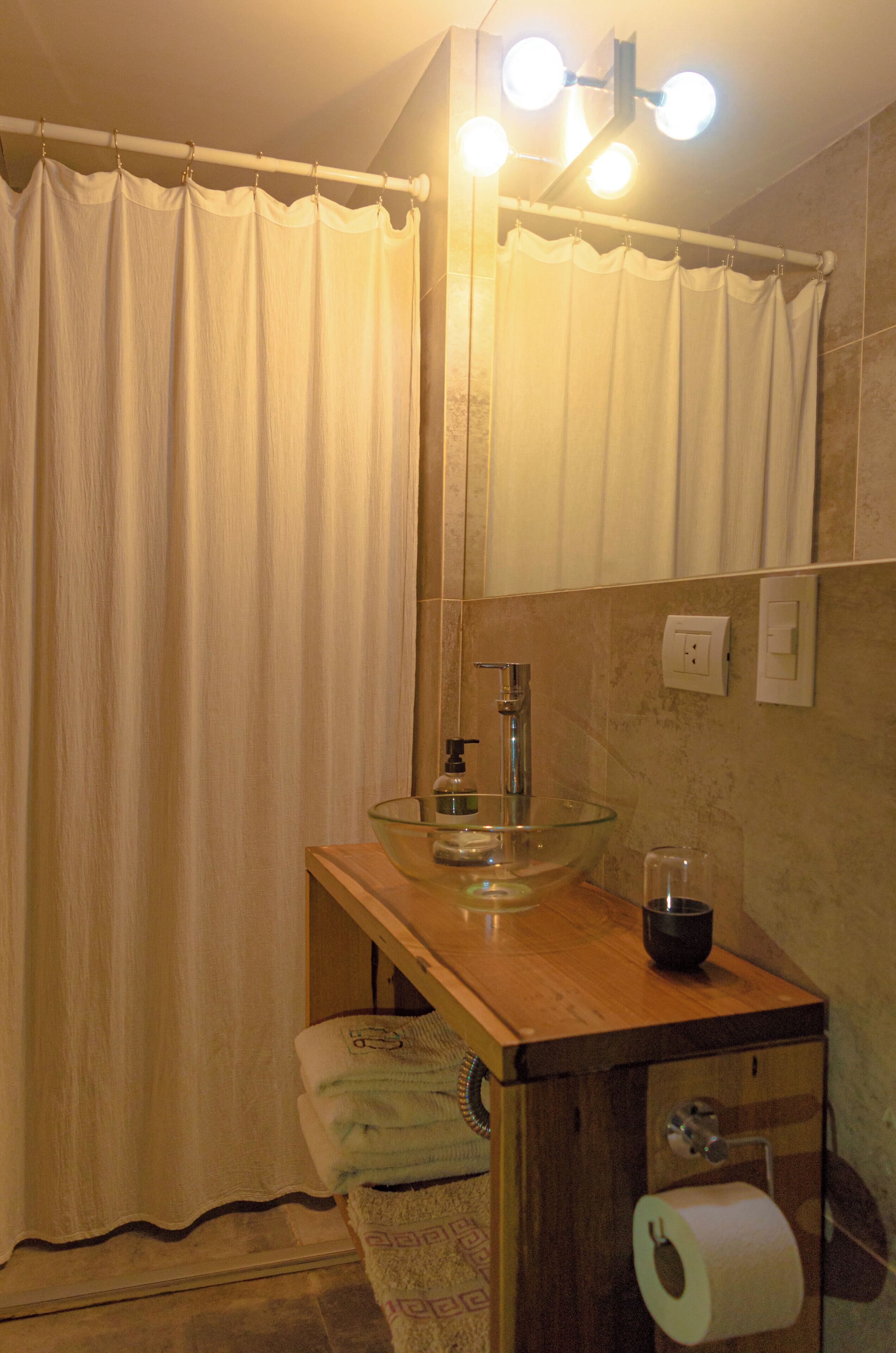 A bathroom with a glass sink, a mirror, a towel rack, and a shower curtain.