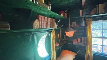 A room with a window, a bed, a shelf with books, and a hanging lamp.
